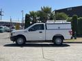 A white 2019 Ford F-150 with a truck bed cover parked on a paved surface with palm trees in the background