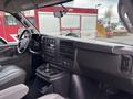 The interior of a 2022 GMC Savana showing the dashboard with controls and a gear shift as well as several cup holders in the center console