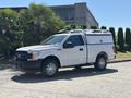 A 2019 Ford F-150 pickup truck with a white exterior and a utility cap on the bed parked on a driveway