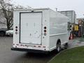 A white 2012 Ford Econoline cargo van with a rear roll-up door and red brake lights parked at an industrial site
