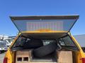 A yellow Chevrolet Silverado 1500 truck with an open rear cover displaying wooden boxes and two black tires inside