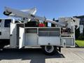 A white 2010 International 4300 equipped with an Altec aerial lift on the side with storage compartments and various tools visible