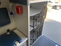 A 2011 Chevrolet Express with an open storage compartment featuring shelves secured by black straps and a red emergency device mounted on the wall