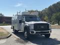 A 2011 Ford F-550 truck with a white body and dual rear wheels featuring a service utility box and overhead ladder rack
