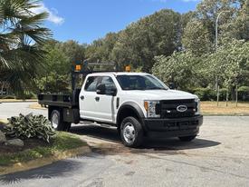 A white 2017 Ford F-550 truck with a flatbed and warning lights parked on a roadway