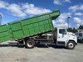 A green 1997 Freightliner FL70 dump truck with its bed raised, showing the truck's side profile and chassis.
