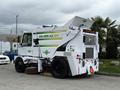 A white 2012 Global M4 street sweeper with green and yellow graphics and a large brush in front for cleaning streets