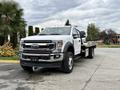 A 2022 Ford F600 truck with a flatbed body in white color featuring prominent front grille headlights and a sturdy design