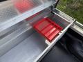 A metal toolbox with a red plastic tray partially pulled out is shown inside a vehicle's storage compartment