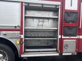 An open storage compartment of a 2006 E-One Typhoon fire truck with metal shelves and hooks for equipment storage