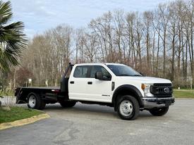 A 2020 Ford F-550 flatbed truck with a crew cab in white color parked with the flatbed visible and no visible cargo