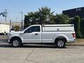 A white 2019 Ford F-150 pickup truck with a cap on the bed parked on a flat surface with palm trees in the background