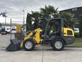 A 2014 Wacker Neuson WL34 wheeled loader featuring a yellow and black design with a front bucket and enclosed driver cabin positioned on a flat surface