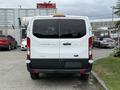 A 2017 Ford Transit T150 XLT viewed from the rear with a white exterior and black lower trim showcasing its large windows and distinctive tail lights