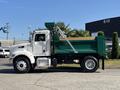 A 2015 Peterbilt 337 dump truck with a white cab and a green bed, facing sideways with its bed raised slightly