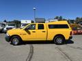 A yellow 2015 RAM 1500 pickup truck with a cap on the bed parked on a lot with other vehicles in the background