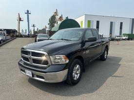 A black 2015 RAM 1500 pickup truck parked at an industrial site with a shiny front grille and five-spoke alloy wheels