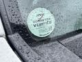 A 2010 Suzuki Carry displaying a round odometer verification sticker on the driver's side window with water droplets on the glass