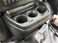 Black plastic center console with three cup holders and buttons above it in a vehicle interior