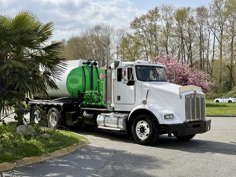A white 1996 Kenworth T800 truck with a green tank on its flatbed, featuring a large chrome grille and dual exhaust pipes