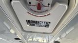 A ceiling view of an emergency exit sign in a vehicle with bilingual instructions to exit the vehicle and a latch indicator