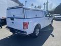 A white 2017 Ford F-150 pickup truck with a hard shell truck cap on the bed is parked with a view of its rear and side
