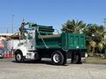 A 2015 Peterbilt 337 dump truck with a green dump bed and a white cab is parked, featuring a hydraulic arm for loading or unloading materials