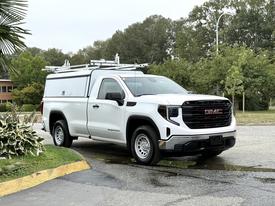 A white 2022 GMC Sierra 1500 pickup truck with a utility cap and roof racks parked on a street