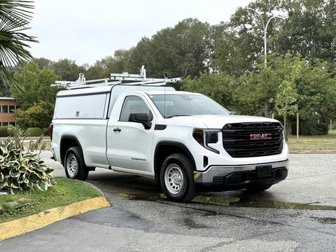 A white 2022 GMC Sierra 1500 pickup truck with a utility cap and roof racks parked on a street