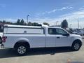 A white 2019 Ford F-150 with a camper shell on the bed and chrome accents parked at a dealership