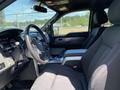 A 2014 Ford F-150 interior featuring a steering wheel with controls a dashboard with gauges and a spacious front seat area with dark fabric upholstery