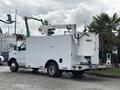 A white 2017 Ford Econoline van with a lift attachment and a utility box on the back parked at an industrial site