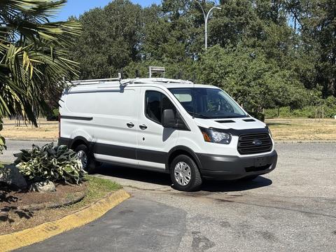 A white 2016 Ford Transit cargo van with sliding side doors and a roof rack parked in a lot