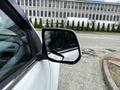 A side mirror of a white 2017 Chevrolet Colorado with a view of the street and buildings reflected in it