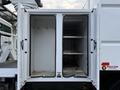 An open storage compartment of a 2015 Freightliner M2 with two shelves and hooks on the inside walls