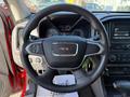 A black steering wheel with a silver GMC logo at the center and control buttons on the left side