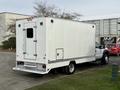 A 2012 Ford F-550 with a white box truck body is parked, featuring a rear door and several lights mounted on the sides. The truck is large and sturdy, suitable for commercial use