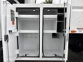 A white 2021 Freightliner M2 106 truck with open storage compartments revealing several shelves and a mostly empty interior space
