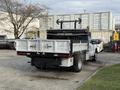 A 2015 Ford F-350 truck with a flatbed and lift gate is parked with its rear facing the viewer displaying a silver finish and dual rear wheels