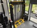 A yellow and black wheelchair lift is installed inside a 2020 Chevrolet Express with a mesh screen and control panel for accessibility purposes
