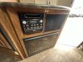 A control panel featuring a radio and a black microwave is mounted on a wooden surface in an RV