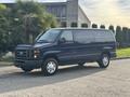 A 2013 Ford E-350 Super Duty van with a dark blue exterior and all-terrain tires parked on a concrete surface
