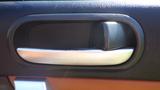 Close-up of a door handle in a 2007 Mazda Miata featuring a silver finish and a textured black background