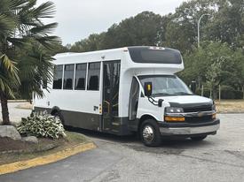 A 2020 Chevrolet Express shuttle bus with a white exterior and large windows parked at an angle with its door open