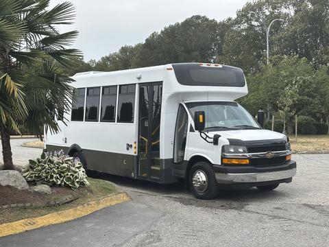 A 2020 Chevrolet Express shuttle bus with a white exterior and large windows parked at an angle with its door open
