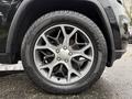 A close-up of a silver five-spoke wheel with a rugged black tire mounted on a 2019 Jeep Grand Cherokee