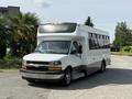 A 2020 Chevrolet Express bus with a white exterior and black accents parked with large windows and a service sign on the front