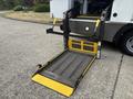 A lowered wheelchair lift from a 2020 Chevrolet Express with black and yellow platform and support arms extended