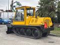 A yellow 2004 Bombardier SW48 tracked vehicle with a cab and rear engine compartment featuring tracks designed for snow and rough terrain