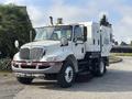 A white 2012 International DuraStar 4300 street sweeper with a large, boxy body and a front-mounted broom attached to the underside of the chassis